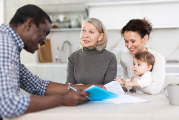 Obraz premium Two female family members with little child trying to reach agreement with man agent sitting opposite to them in the kitchen