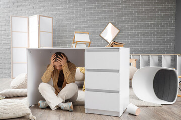 Young woman hiding under desk at home during earthquake