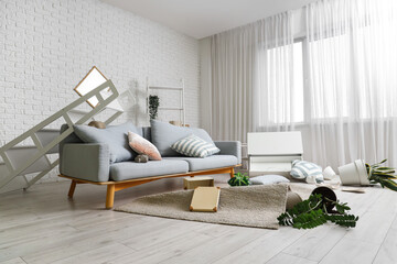 Interior of messy living room with sofa and overturned things after earthquake