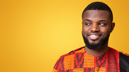 Obraz premium Interested black guy smiling and looking at free space, yellow studio background, panorama