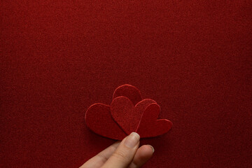 Mano sujetando tres corazones juntos con textura granulada de goma Eva roja