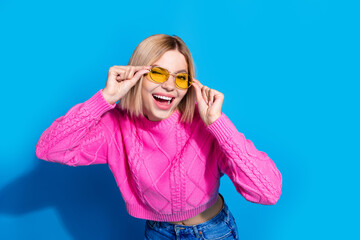 Portrait of nice young woman touch sunglass eye wink wear pink sweater isolated on blue color background