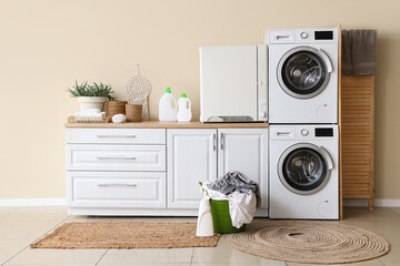 Interior of home laundry room with washing machines, counter, dryer and basket with clothes