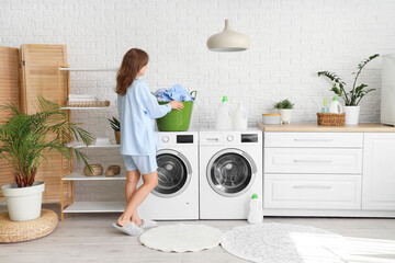 Young woman with laundry basket on washing machine in room