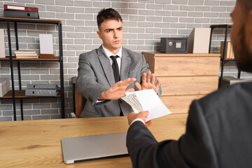 Young businessman refusing to take bribe at table in office. Corruption concept