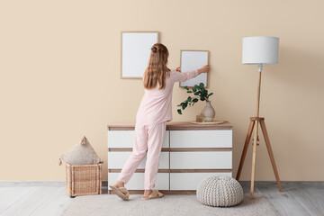 Woman hanging blank photo frame on beige wall