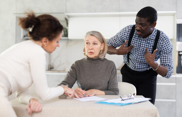 Competitive middle-aged man and woman conflicting and old woman writing testament sitting at...