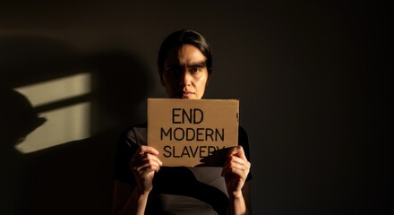 Woman holding sign against modern slavery in dark setting