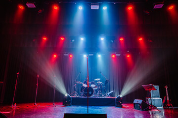 A concert stage with colorful red and blue lighting, microphones, a drum set, and guitars, ready for a live music performance.