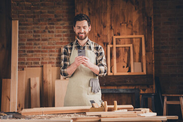 Photo of attractive cool craftsman dressed uniform chatting modern device indoors garage home house