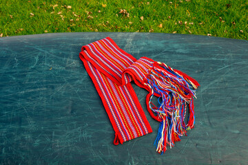 ceinture fléchée (traditional pattern) replica of the woven sash worn by voyageurs during the fur trade on overturned green canoe  room for text