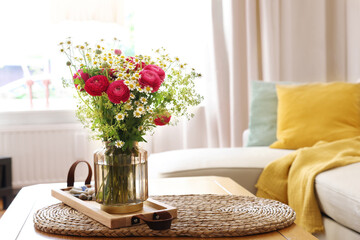 Beautiful ranunculus flowers and chamomiles in vase on table indoors