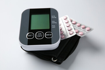 Blood pressure measuring device and pills on white background, closeup