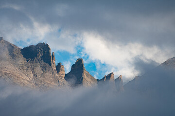 Majestic mountain peaks emerge from morning mist under a bright blue sky in a remote wilderness area, showcasing nature's serene beauty