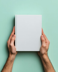 Obraz premium A pair of hands holding a blank book against a mint green background.