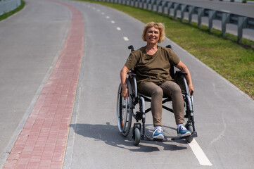 Obraz premium Happy elderly woman on a wheelchair rides along a bike path. 