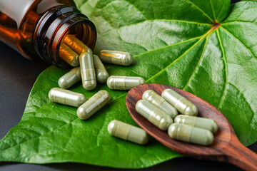 Pile of herbal capsules on wooden spoon with herbs and green natural Betel pepper leaf background
