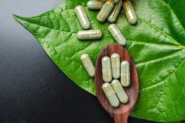 Pile of herbal capsules on wooden spoon with herbs and green natural Betel pepper leaf background