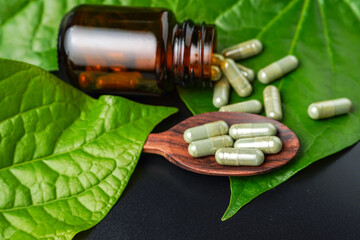 Pile of herbal capsules on wooden spoon with herbs and green natural Betel pepper leaf background