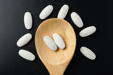white Pills Medicine tablet capsules in a wooden spoon blister pack on a black background