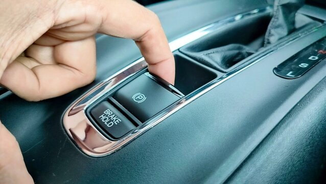 Finger pressing the electronic parking brake button on luxury car. Electric electronic Parking Brake with Auto-hold on modern vehicle