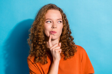 Photo of youth thoughtful funny doubtful girl with curly hairstyle wearing orange t shirt looking novelty isolated on blue color background