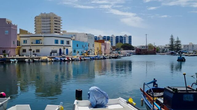 View of clear sea water, small fishing boats and colorful buildings in the harbor of Bizerte, Tunisia on a sunny day