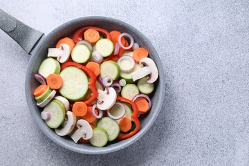 Frying pan with mix of fresh vegetables and mushrooms on grey table, top view. Space for text