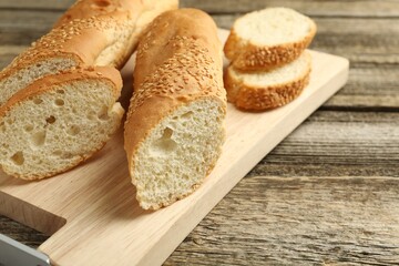 Cut fresh baguette with sesame on wooden table, closeup. Space for text
