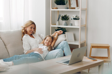 Obraz premium Mother and daughter bonding while watching a video on a laptop together on a cozy living room couch