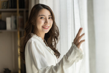 Beautiful young asian woman looking out window with a fresh and happy expression, serene mood, peaceful morning, joyful and relaxed, bright sunlight, cheerful atmosphere, optimistic and vibrant moment