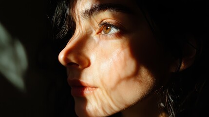 Fototapeta premium Close-up portrait of a young woman looking away, her face illuminated by sunlight streaming through a window.