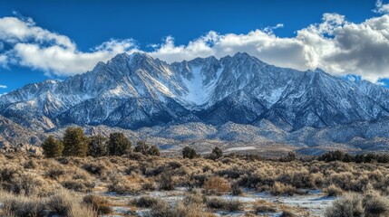 Majestic snow-capped mountain range with a blue sky and white clouds.