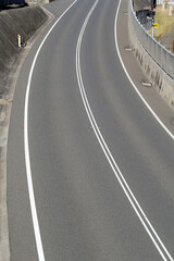 Curved asphalt bitumen road with white lane markings and concrete barriers