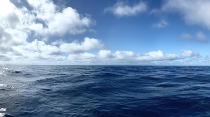 Obraz premium Vast Tranquil Ocean Surface Under Clear Blue Sky with Fluffy White Clouds, Perfect for Travel and Nature Themes in Stock Photography