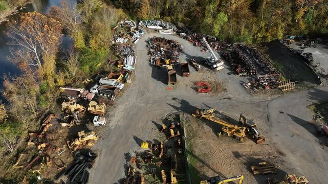Aerial tilt down of Exkavators trucks and other industrial vehicles parking outdoors in suburb oi american town. Forest trees in autumn season.