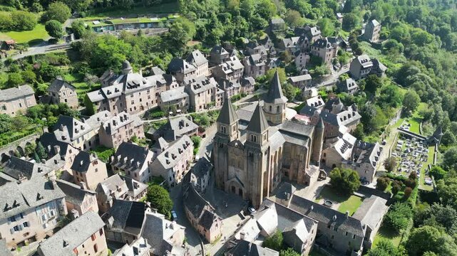 Drone aerial view in France countryside small old medieval town and a cathedral surrounded by a green mountain forest flying over in Conques