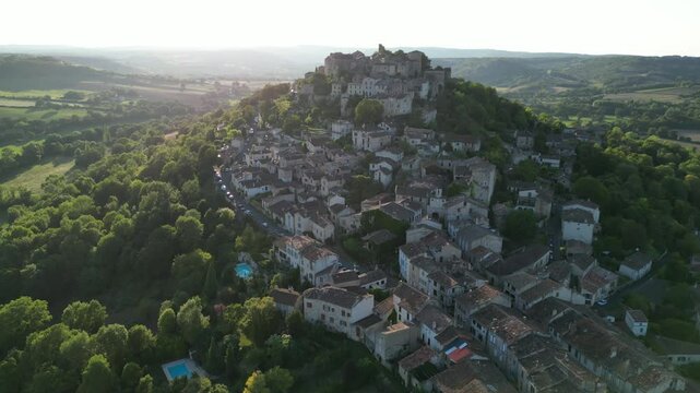 Drone aerial view in France countryside small old medieval brick town on a mountain top surrounded by green fields zooming out on a sunny day in Cordes Sur Ciel