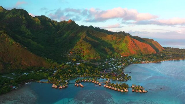 Golden hour sunny sunset water bungalows Cooks Opunohu Bay Moorea island French Polynesia aerial drone Mount Mauaroa Tohivea Rotui clouds boats lagoon coral reef waves Pacific Ocean backwards pan up