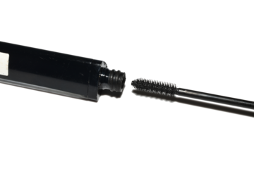 A bottle of black mascara and a brush are lying on the table.