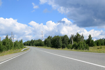 Empty highway surrounded by forest. Beautiful summer landscape, white clouds on a blue sky.