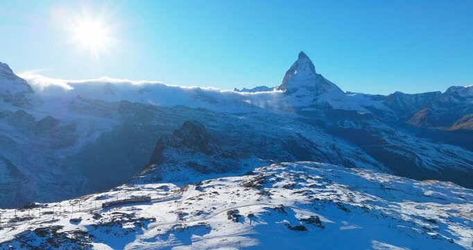 Aerial drone footage of Gornergrat bahn railway running towards summit station with Matterhorn mountain peak background in Zermatt on a sunny winter day. Swiss Alps, Switzerland travel journey trip.