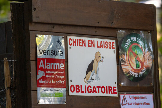 France, 11 August 2024: Signs on a wooden fence including "Chien en laisse obligatoire" and security alarm warning.