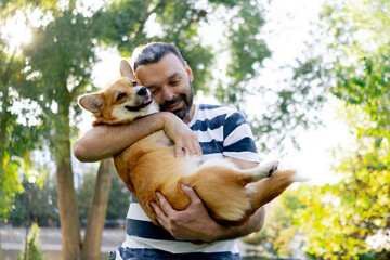in the park in the summer the owner in a striped T-shirt holds and hugs pressing head to muzzle in...