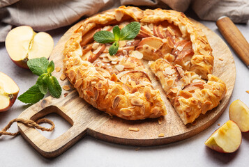 Delicious homemade apple galette with almond flakes and fresh mint on rustic wooden board