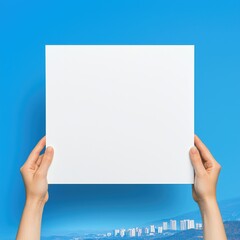 Obraz premium Hands holding blank white paper against a blurred city skyline and blue sky.
