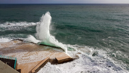 A stunning view of waves crashing dramatically against the coastal structures in Funchal, Madeira, showcasing the raw beauty of the Atlantic Ocean