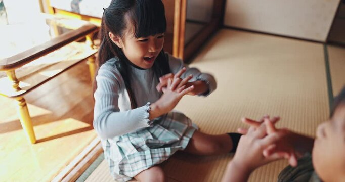 Children, home and play clapping game for bonding, love and Japanese family relax in living room. Kids, pat hands and together for fun with Asian siblings, sister and brother on floor for development