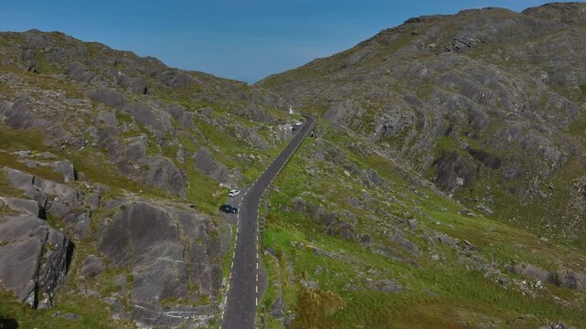 Healy Pass, County Cork, Ireland, September 2024. Drone pushes forwards following the road along the rocky cliff side building to a panoramic reveal of Glenmore lake in County Kerry.