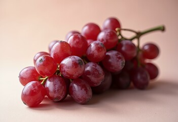 Bunch of glossy red grapes with green leaves on beige background